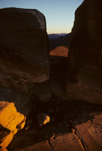 South-westward view at sunset, through natural cleft in highly geometric granite formations standing on flat, cracked rock base on the summit of Mt Sinai.