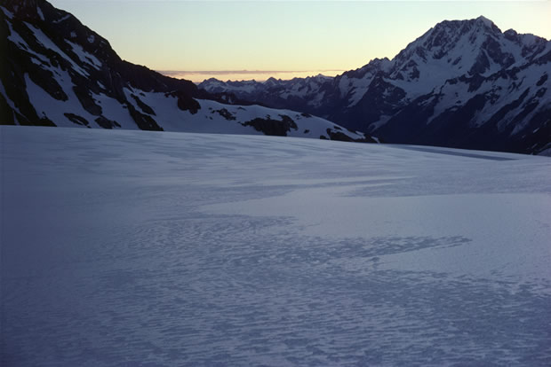 Tasman Glacier: southward view of lower neve in evening light disclosing flow lines in "firn", the thin crust formed by the melting followed by the re-freezing of as yet uncompacted surface snow. Malte Brun range on left. Mt Cook on right.