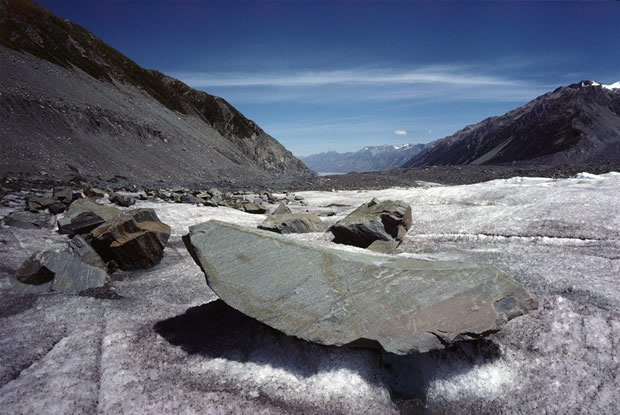 Tasman Glacier: southward view of lower reaches. Ice-scored boat-shaped boulder in foreground. Ben Ohau Range on right; Burnett Mountains on left.