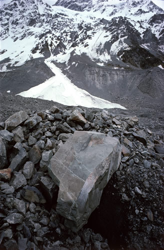 Tasman Glacier: facetted boulder on surface moraine of lower reaches of glacier. Lateral moraine with fan-shaped ice-spill from Main Divide of Southern Alps in distance.