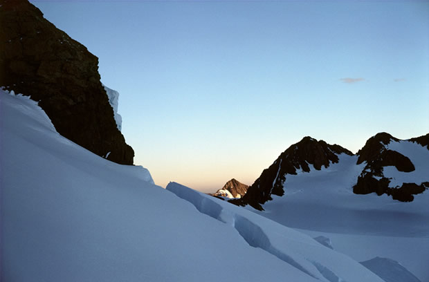 Tasman Glacier: westward evening view across crevassed upper neve, through Tasman Saddle to sunlit peak of distant Mt Sibbald.