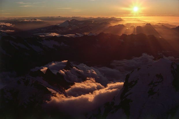 Southern Alps: westward view at sunset, from above the Baker Saddle on the Main Divide. The summit of Mt La Perouse, located 5 km directly west of Mt Cook, is seen mid-right; Dilemma Peak, lower left. On the horizon in the mid-left of the frame appears the solitary peak of Mt Aspiring (9,951 ft). Close below and to the right of Mt Aspiring are seen Mt Brewster (8,448 ft) on right and Mt Armstrong on left.